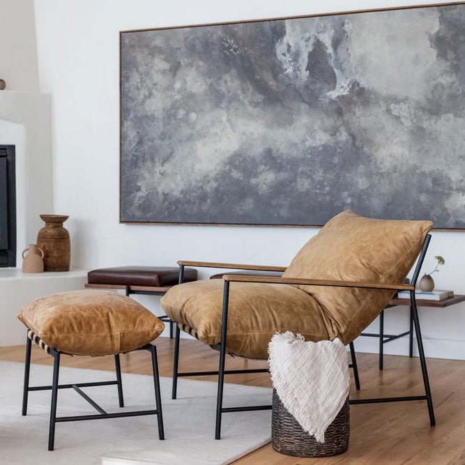 Modern living room with a tan leather Denver Modern lounge chair and matching ottoman, black metal frame, and neutral decor, set beside a fireplace and large abstract wall art.