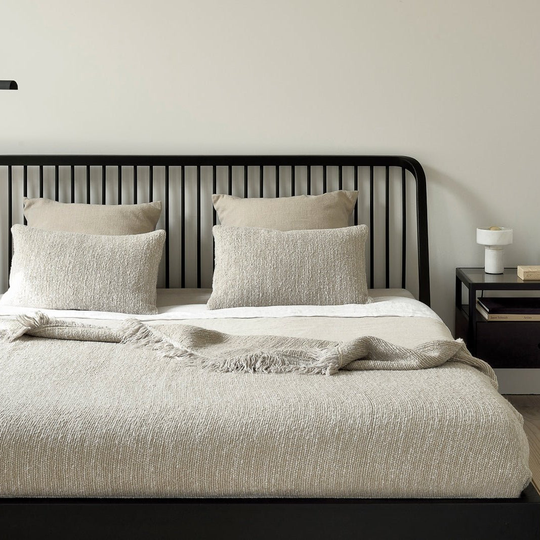 Modern bedroom with black spindle headboard bed, neutral bedding, and black metal nightstand, styled with a white lamp and minimalist decor against a light wall backdrop.