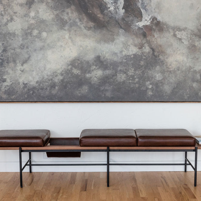 Modern Denver Modern living room bench with brown leather cushions, black metal frame, and integrated side table, placed under large abstract wall art on a hardwood floor.