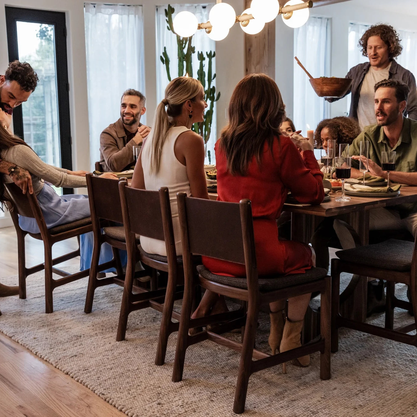 Modern dining room with wood dining table and chairs, featuring a group enjoying a shared meal in a warm, contemporary setting.