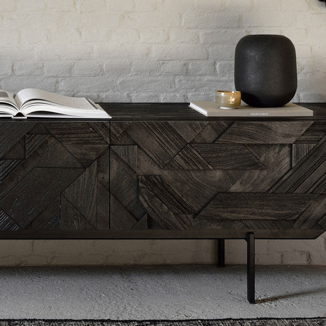 Dark wood Denver Modern media console with geometric inlay pattern, styled with an open book, black vase, and small cup, set against a white brick wall in a modern living space.