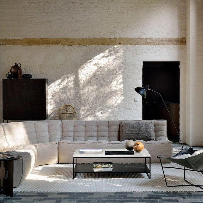 Spacious living room with a cream upholstered N701 modular sectional sofa, black metal coffee table, modern side table, and butterfly chair, set against textured white walls with tall windows.