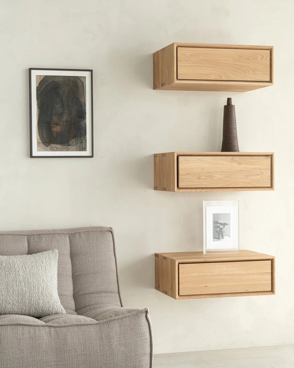 Light wood wall-mounted bedside table with single drawer, displayed above upholstered sofa.