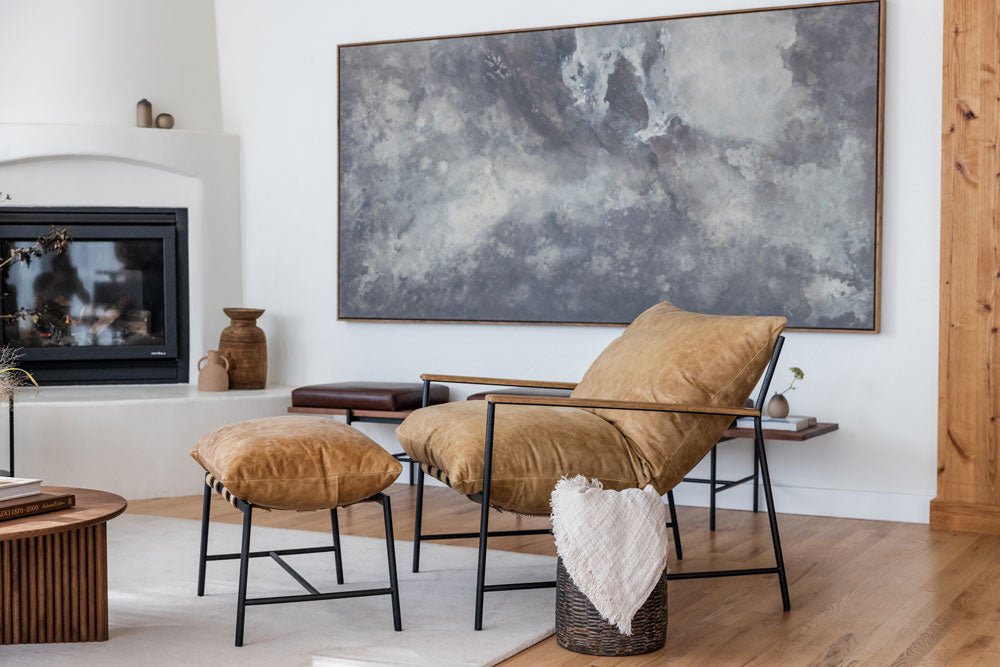 Modern living room with a tan leather Denver Modern lounge chair and matching ottoman, black metal frame, and neutral decor, set beside a fireplace and large abstract wall art.