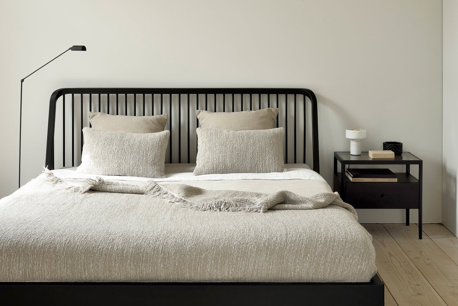 Modern bedroom with black spindle headboard bed, neutral bedding, and black metal nightstand, styled with a white lamp and minimalist decor against a light wall backdrop.