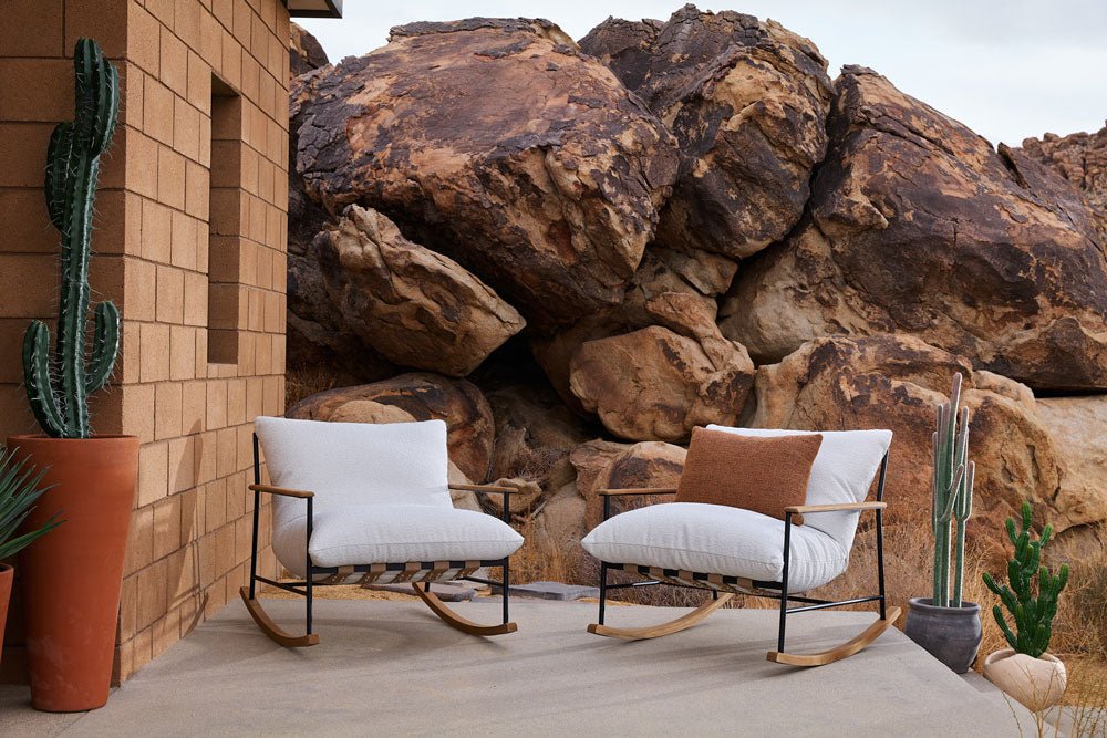 Modern Outdoor Vail Rocking Chairs with white cushions and wood-accented frames, set against large desert boulders with potted cacti.