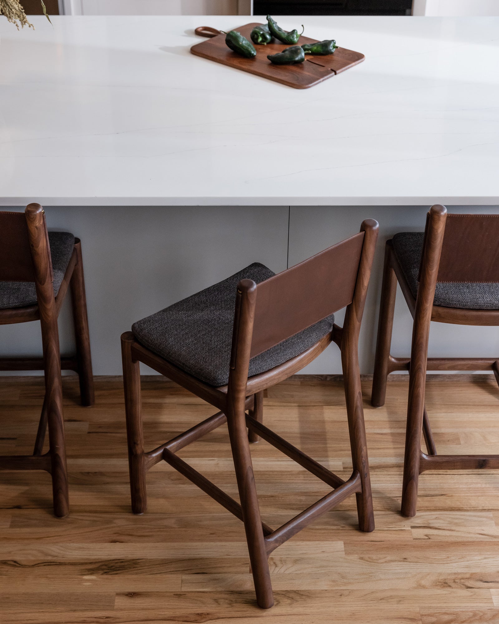 Wooden bar stools with dark cushions in a kitchen setting.
