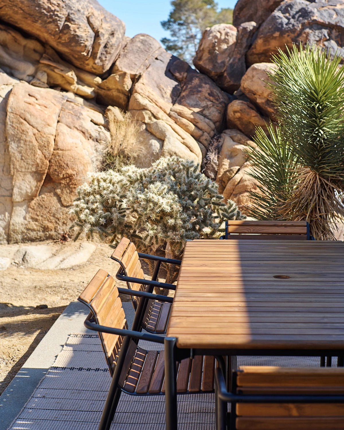 Outdoor Strata Dining Table with matching dining chairs on a desert patio, featuring a slatted wood top and steel frame in a natural landscape setting
