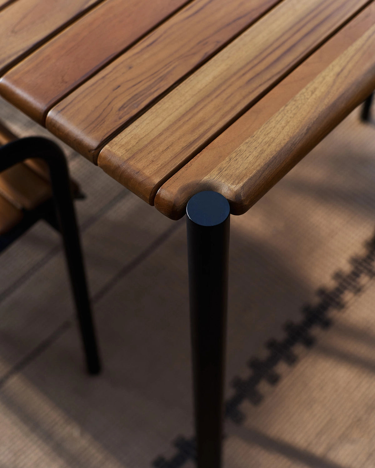 Close-up of the Outdoor Strata Dining Table showing solid wood slat construction and black powder-coated steel leg detail