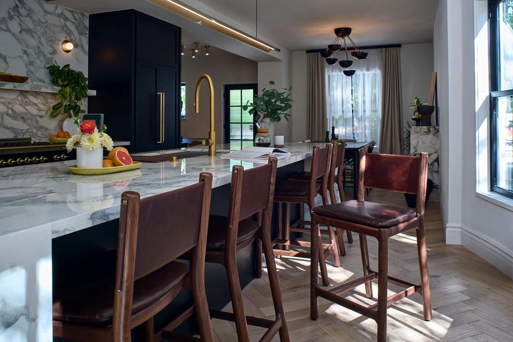 Modern kitchen with marble island, Avon Counter Stools, and large windows.