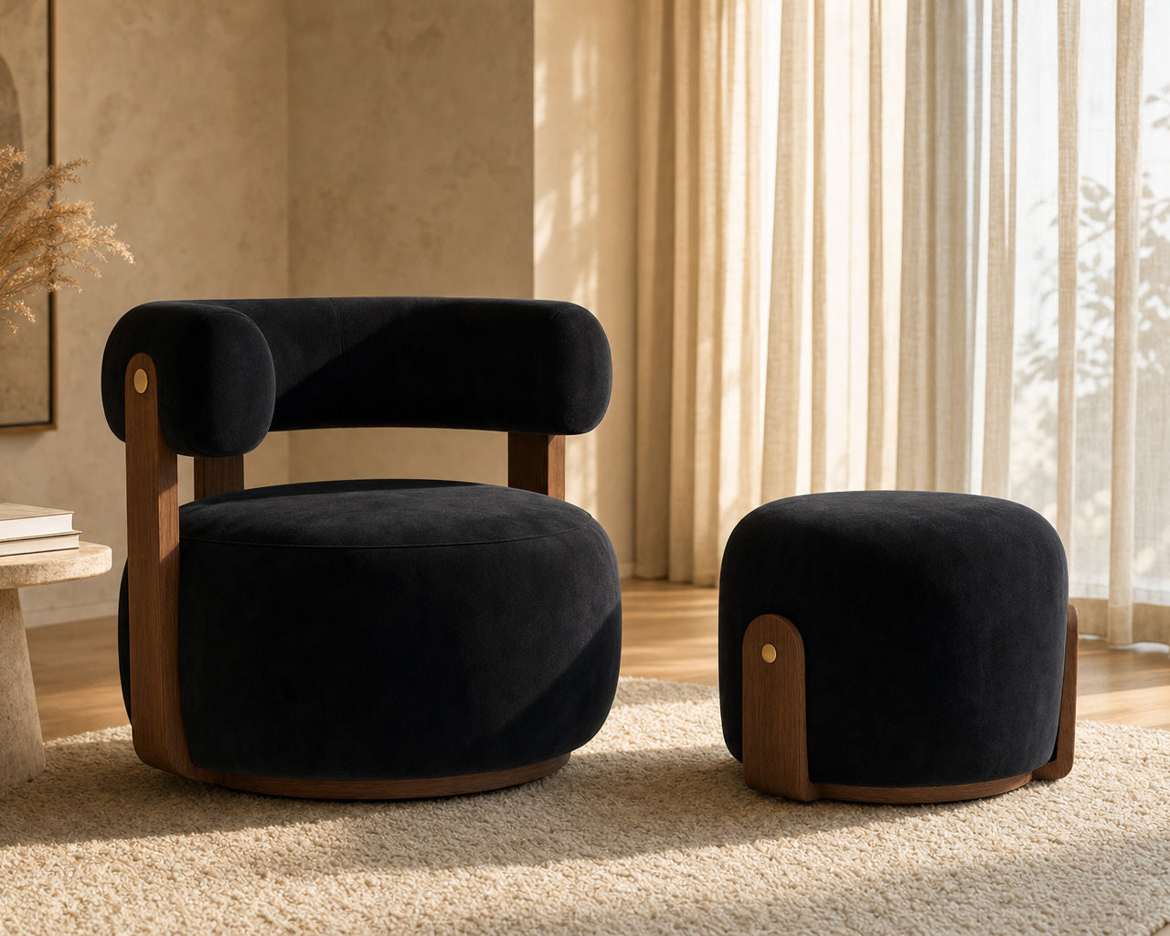 A modern black velvet armchair with curved wooden legs sits beside a matching round ottoman in a warm, sunlit room with beige walls and sheer curtains.