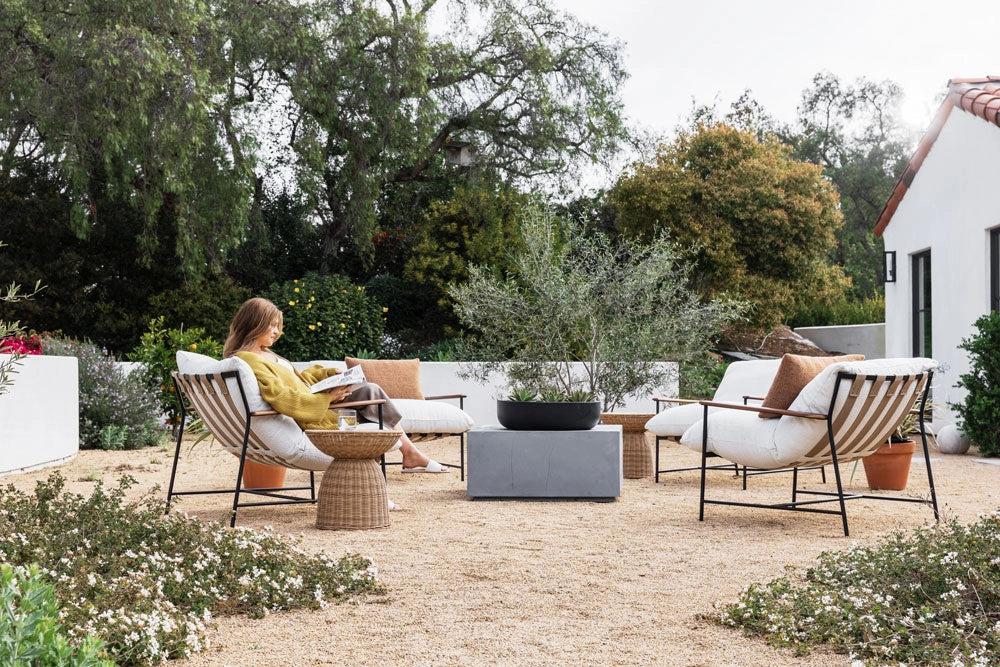 Outdoor Vail Lounge Chairs in a circle around a coffee table with a woman reading. 