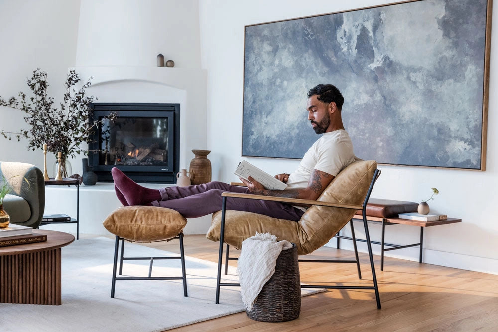 Man reading a book in a Vail Lounge Chair in a modern living room with a fireplace and large abstract painting.
